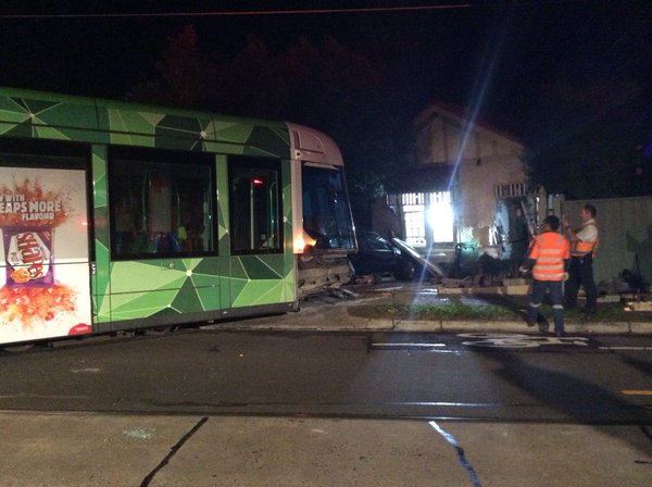 Photo of a battered-looking tram whose front is sitting in a driveway. Behind it is a damaged house.