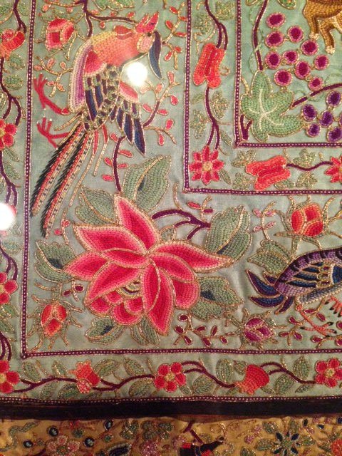 close up of embroidered table dressing; a beaded flower is surrounded by beards, and a small border of different flowers